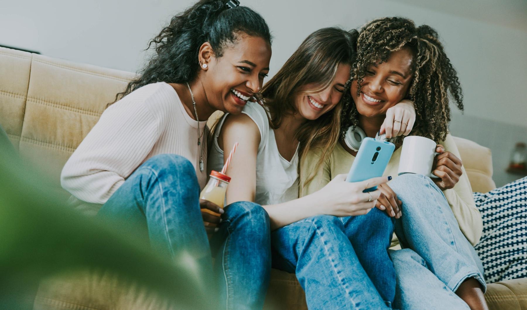 a group of women sitting on a couch looking at a cell phone
