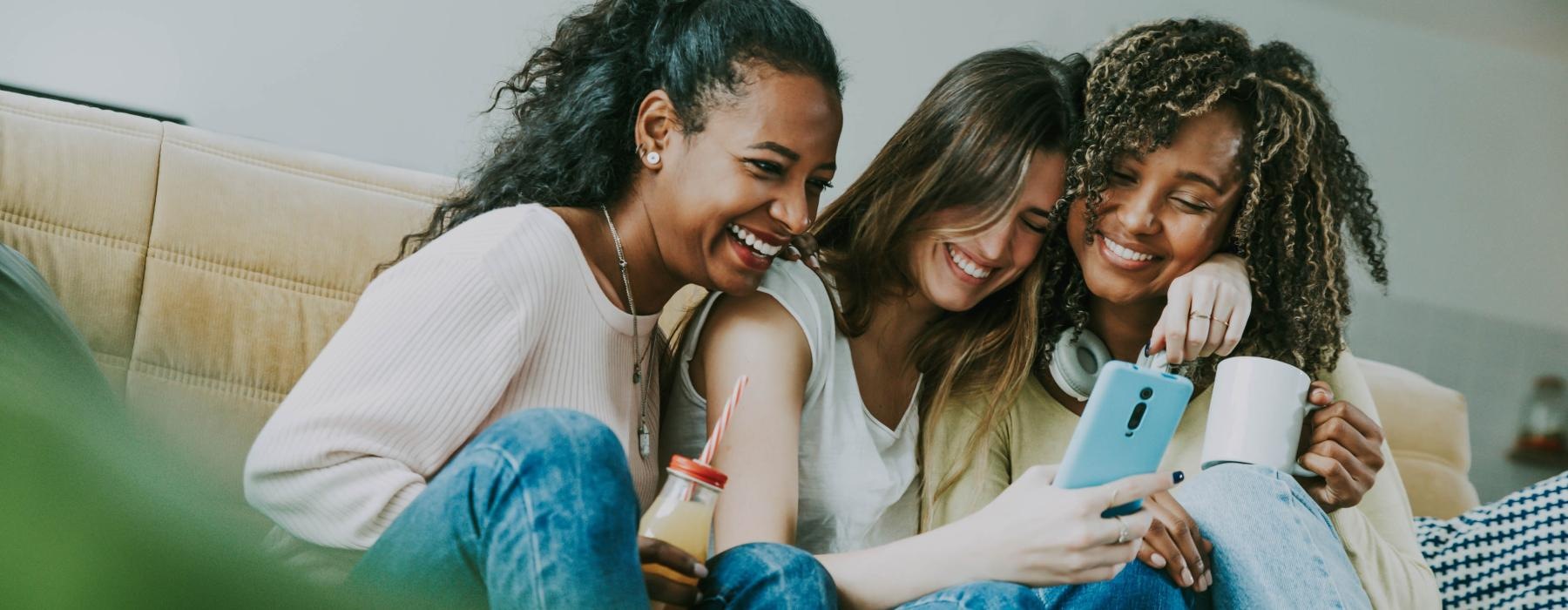 a group of women sitting on a couch looking at a cell phone