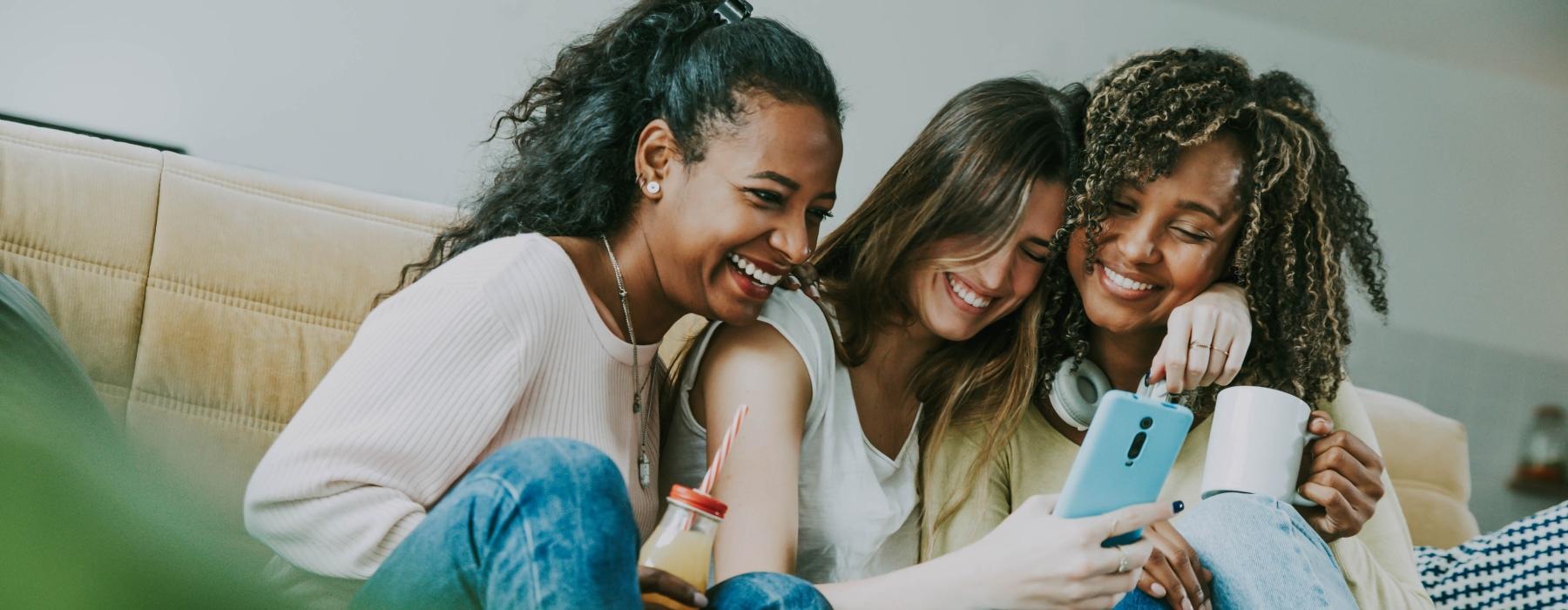 a group of women sitting on a couch looking at a cell phone